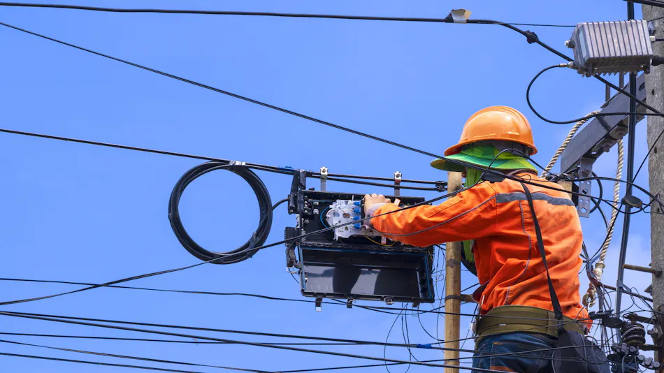 Aerial fibre technician connecting fibre inside an aerial distribution box beside overhead telecommunications lines