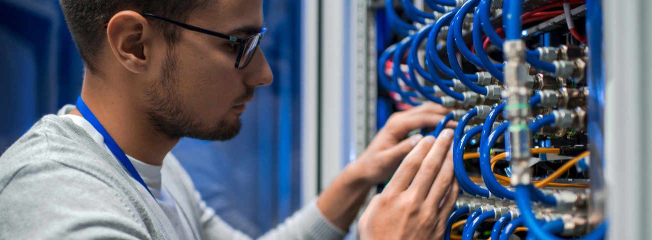 Network technician patching blue data cables into equipment inside a network rack