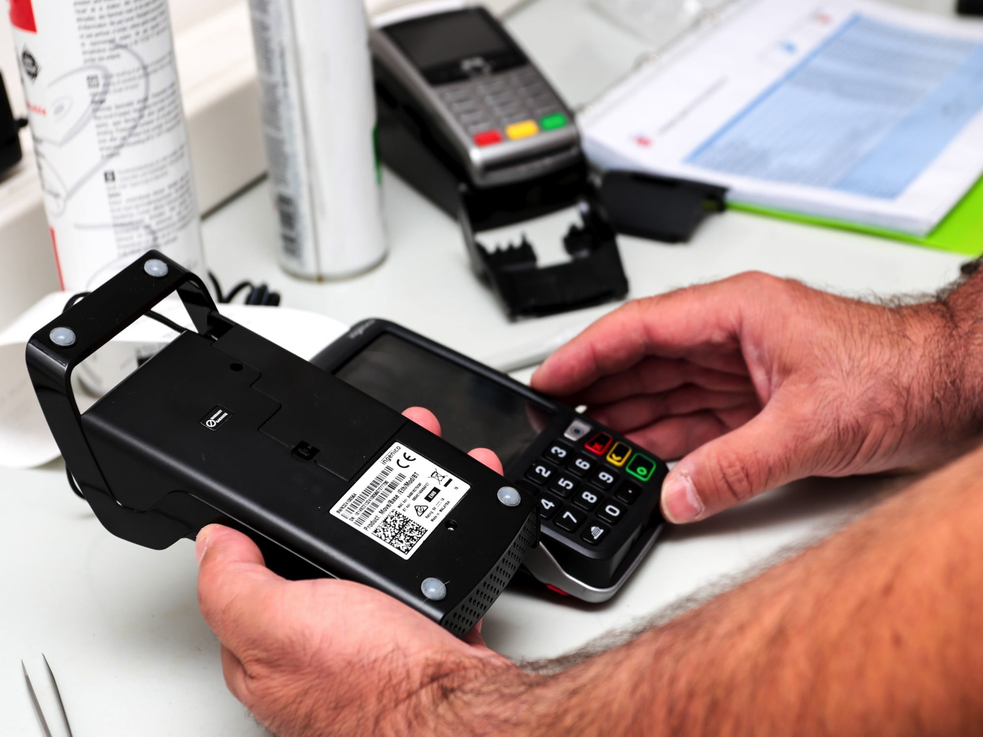Technician servicing an opened payment terminal and pin pad on a workbench