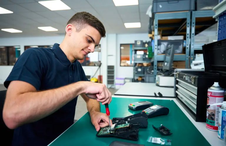 Technician opening and repairing a pin pad payment terminal on an electronics workbench