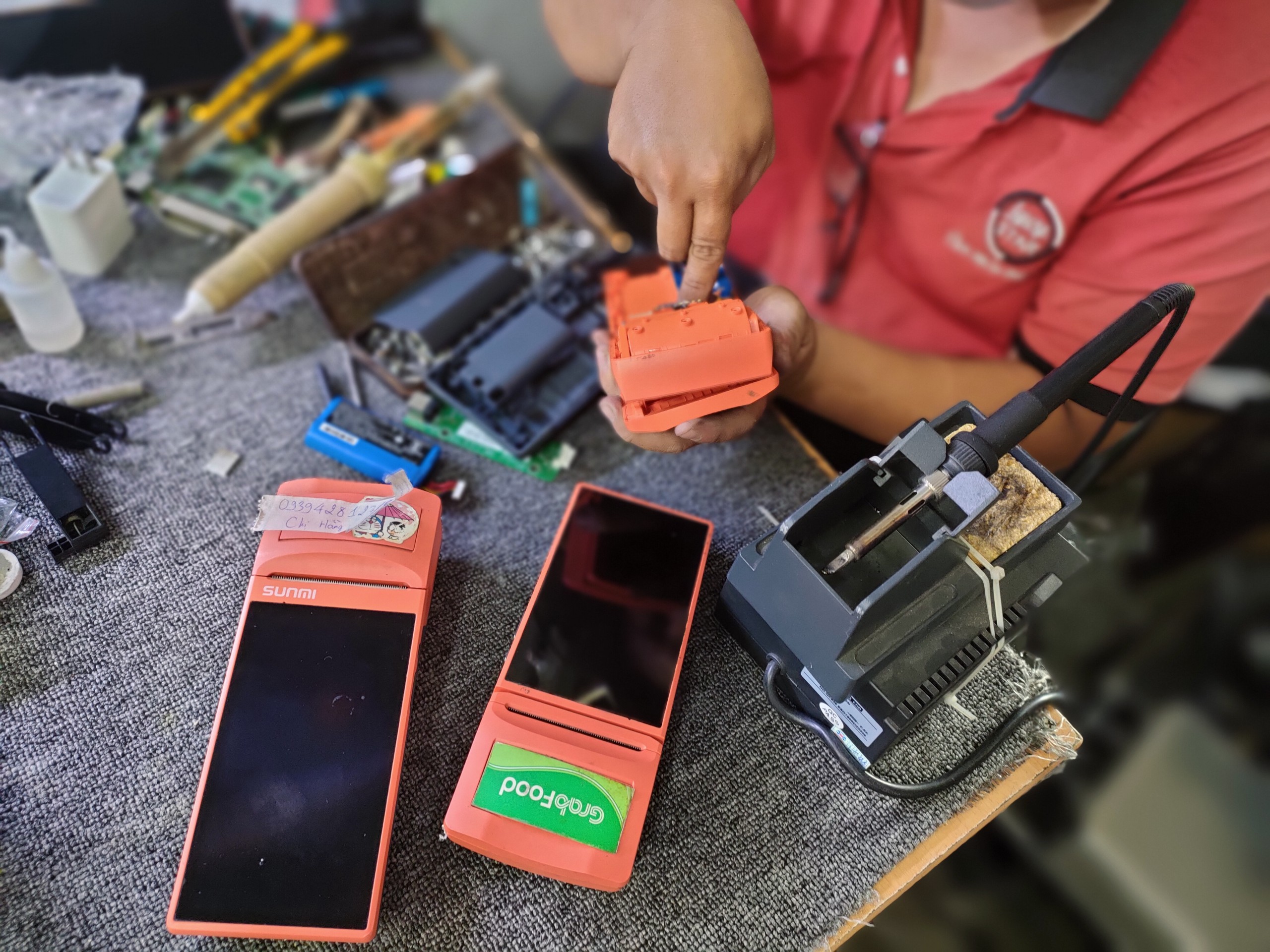 Technician repairing POS payment devices with soldering equipment on a workbench