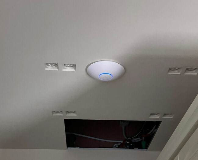 Wireless access point mounted on a ceiling, powered on with its status light glowing